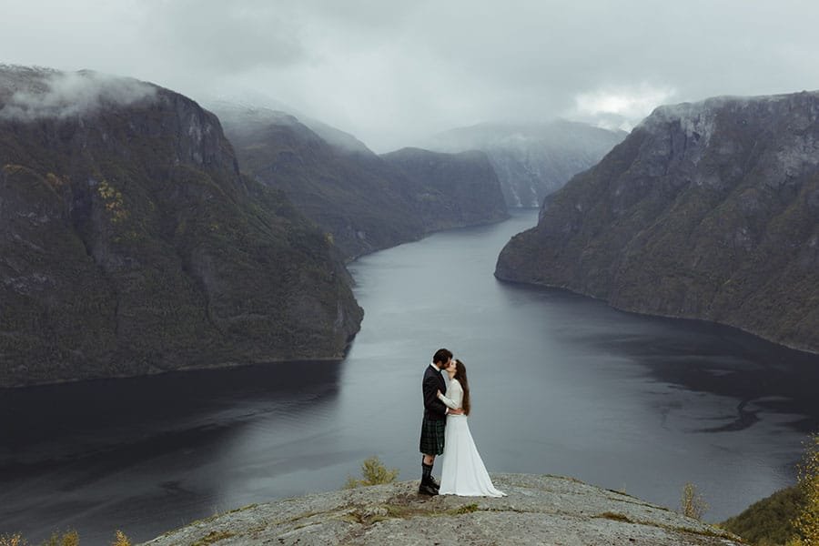 bride and groom are kissing with a norwegian fjord behind them