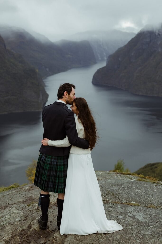 the groom are kissing the bride and they are enjoying the view of the fjord